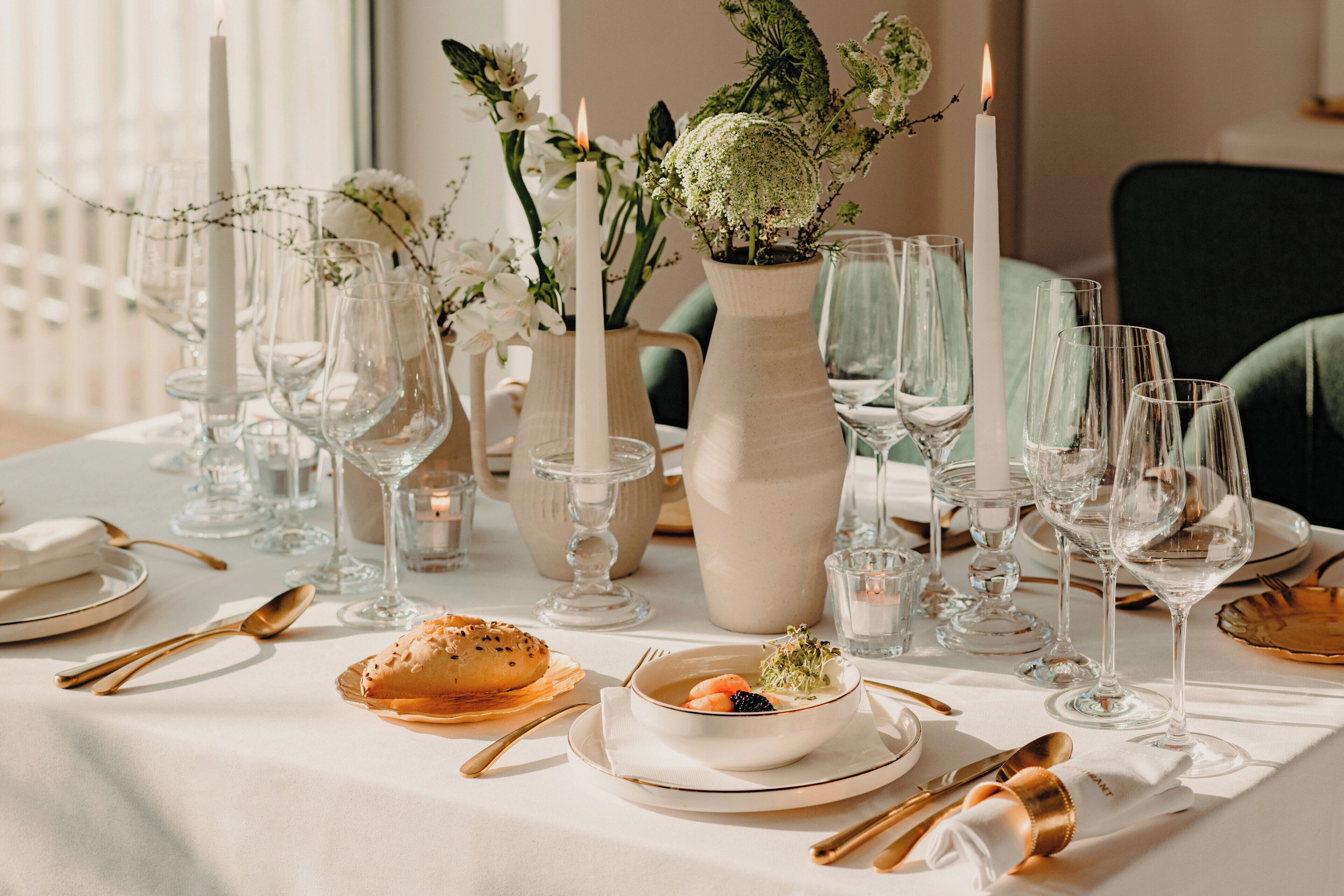 A table set for a meal with clear glassware, white plates, and gold cutlery.