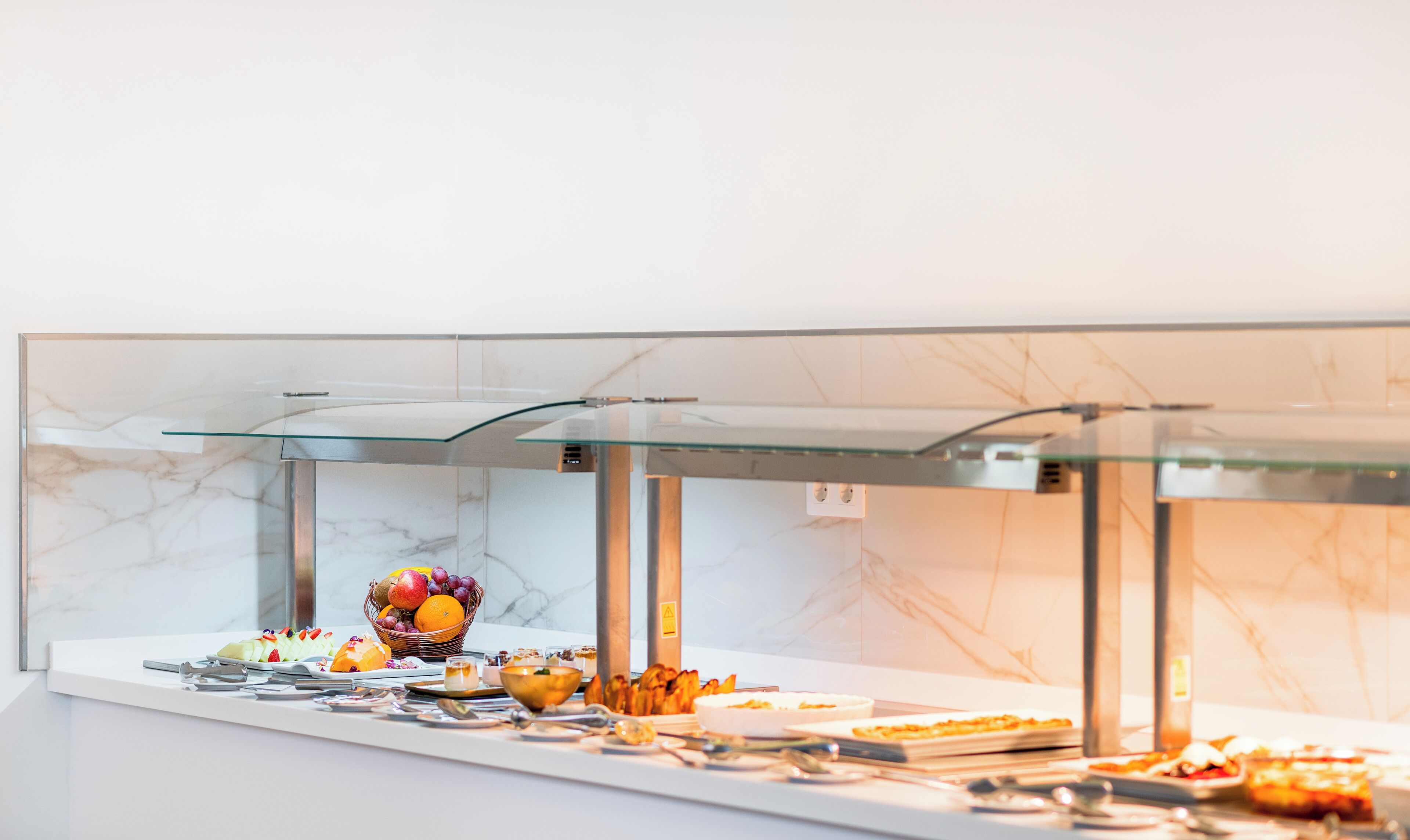 A buffet with various food items, including fruits, vegetables, and prepared dishes, displayed in a glass-fronted serving area.