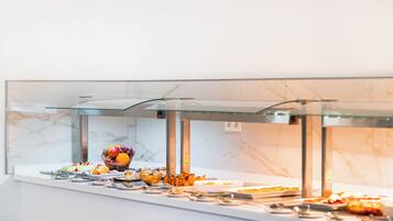 Un buffet proposant une variété d’aliments, notamment des fruits, des légumes et des plats préparés, présentés dans un espace de service vitré.