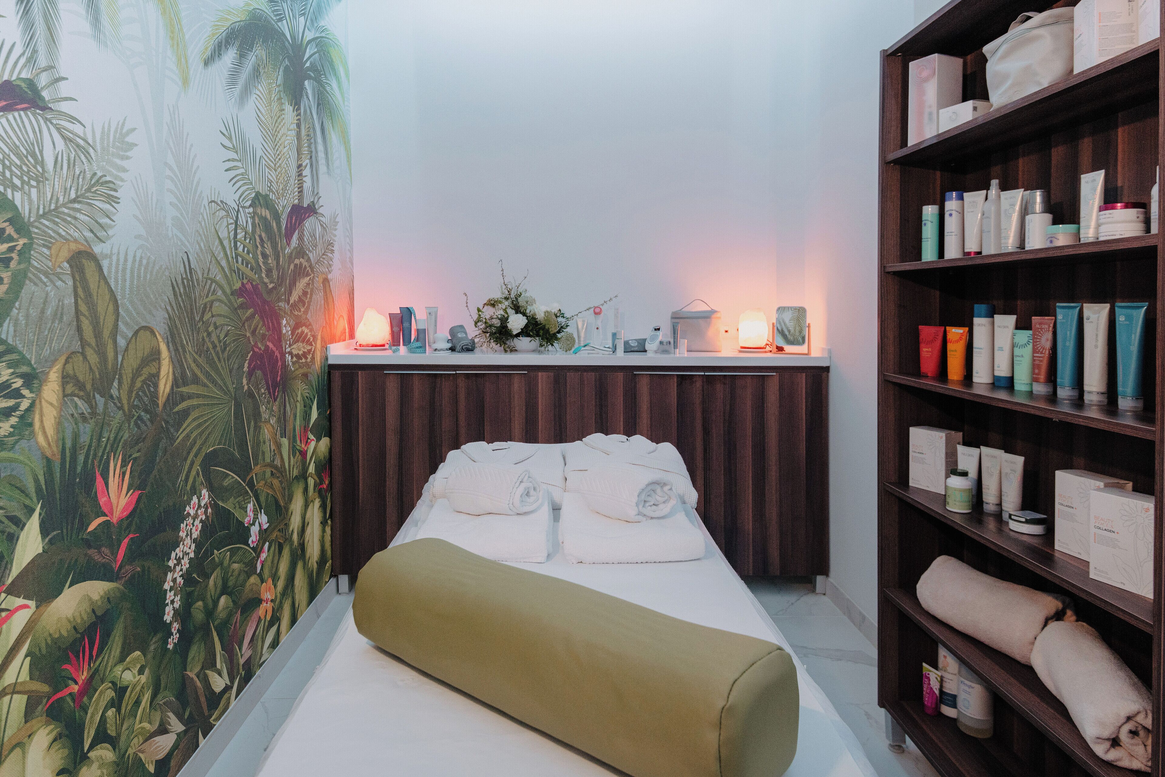 Ein Zimmer mit einem Bett, einem hölzernen Ablagefach mit Pflegeprodukten und einem tropischen Wandbild.
