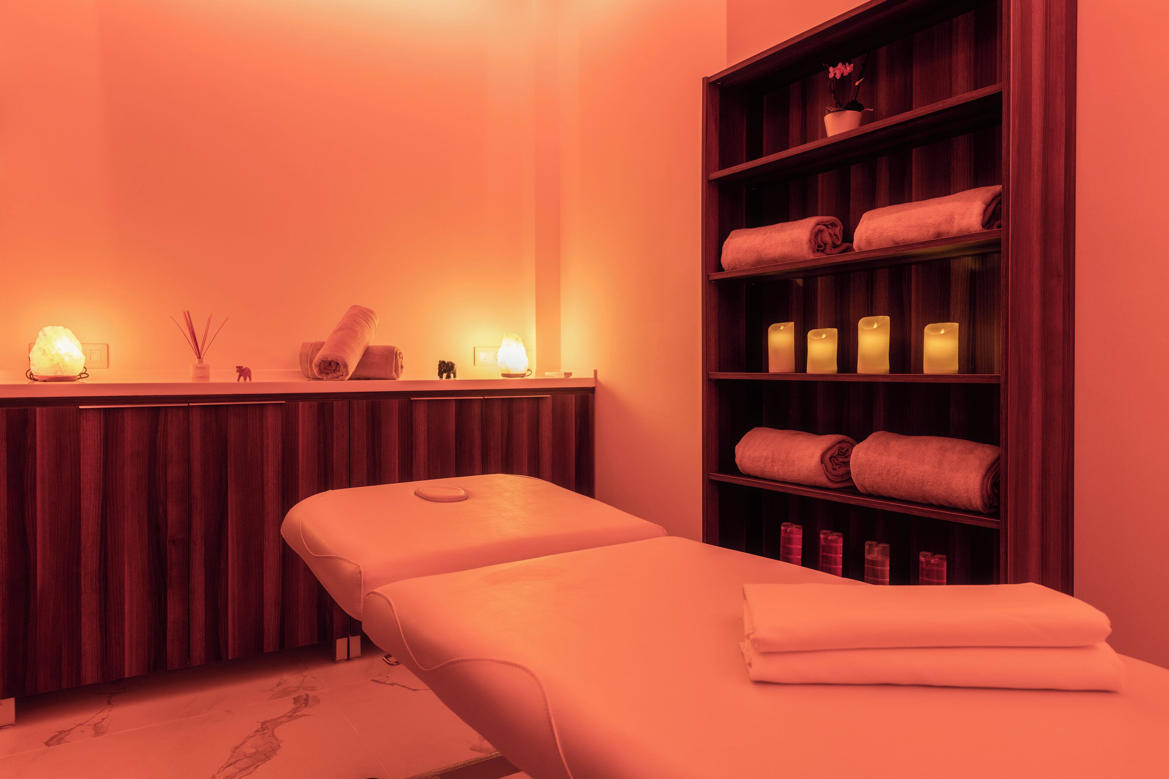 Un cuarto de spa con una camilla de masaje, repisas con toallas y velas.