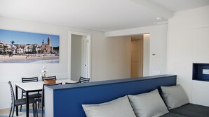 A modern room with a dining area, a sofa, and a view of a beach with buildings. - Sunway Arizona (Sitges)