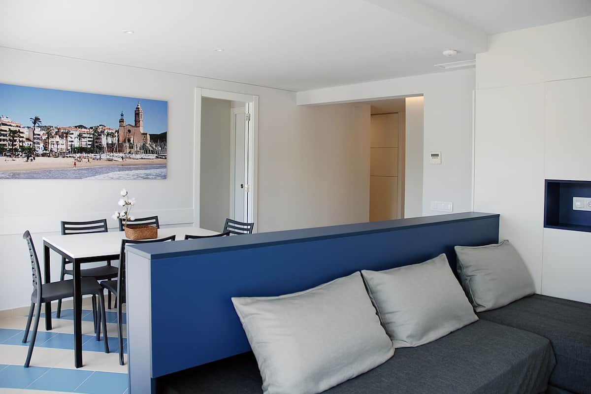 A modern room with a dining area, a sofa, and a view of a beach with buildings.