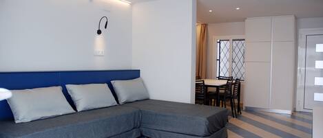 A modern room with a grey sectional sofa, a dining area with a table and chairs, and a white wardrobe.
