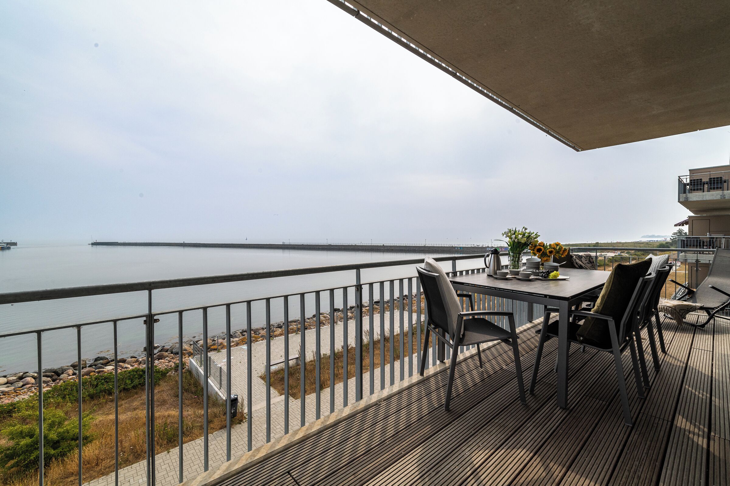 A balcony with a view of the water, a table with chairs, and a railing.