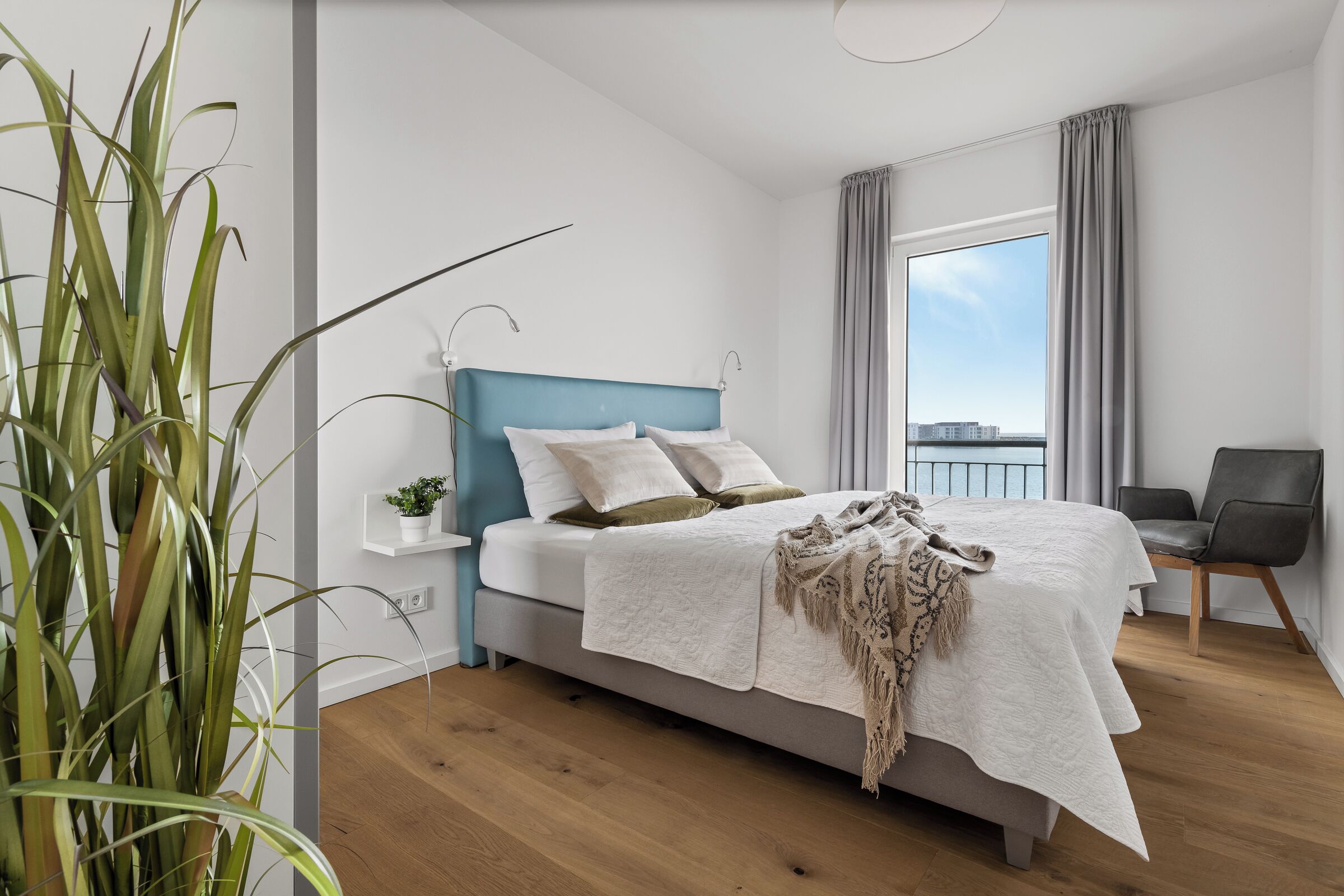 Une chambre à coucher moderne avec un lit, une plante sur la table de chevet, une chaise et une vue sur la ville.