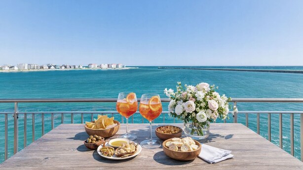 A table with snacks, drinks, and a floral arrangement overlooking a coastal view.