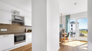 Une cuisine moderne avec des meubles blancs, un four encastré et un coin repas comprenant une table et des chaises.