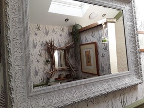 A mirror with an ornate frame, a wooden picture frame, and a small plant on the wall.