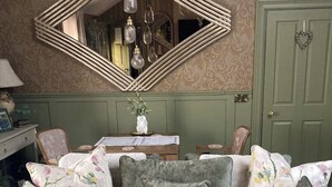 Un salón acogedor con un sofá verde, cojines estampados y un florero verde con flores blancas sobre una mesa.