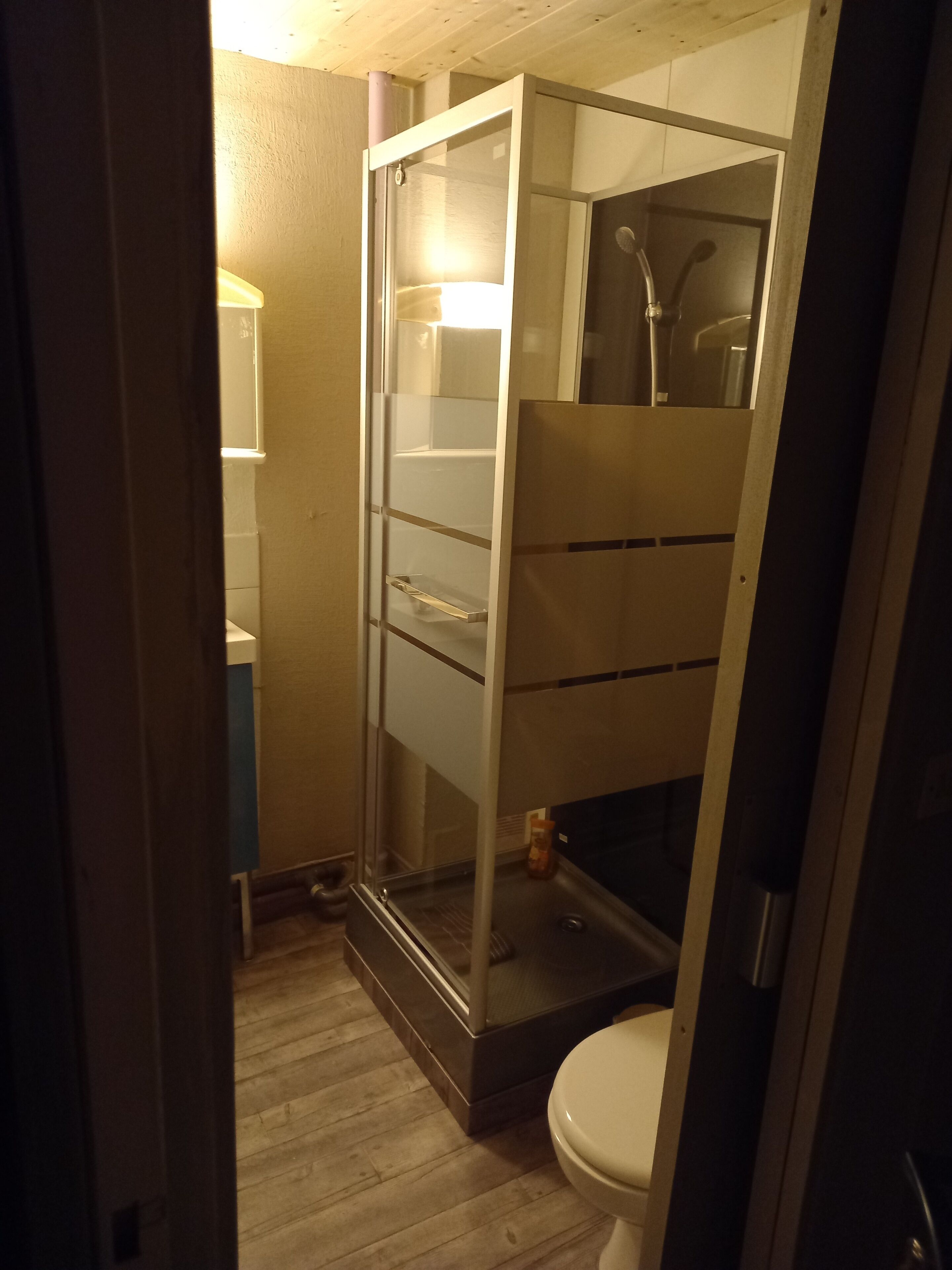 Un baño pequeño con cabina de ducha de vidrio, inodoro blanco y suelo de madera.