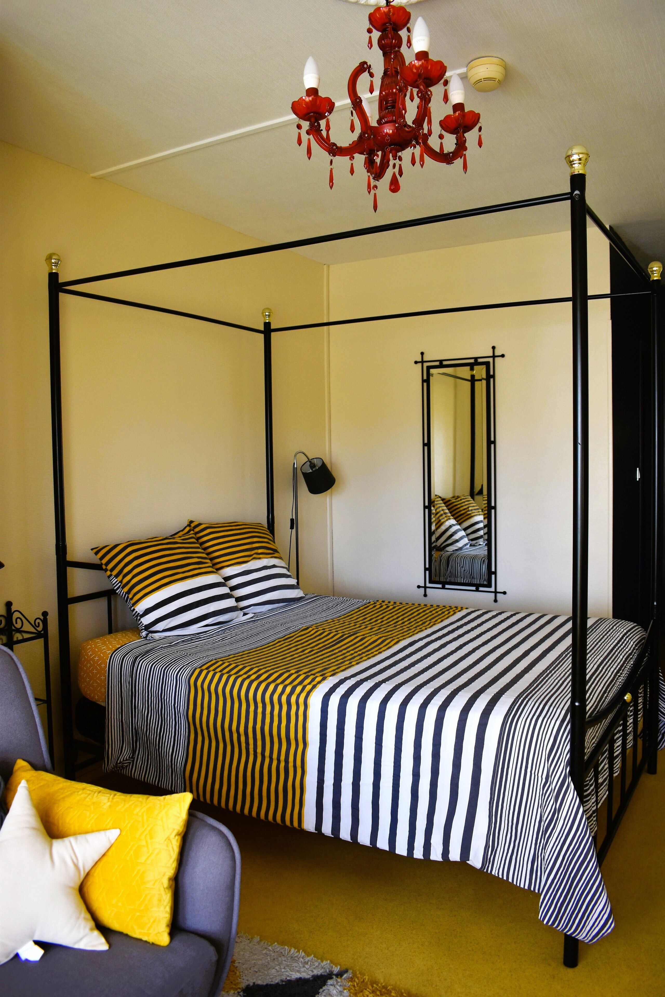 Una cama con dosel y ropa de cama a rayas, un plaid amarillo y un espejo en la pared.