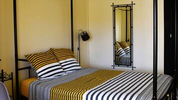 Una cama con dosel y ropa de cama a rayas, un plaid amarillo y un espejo en la pared.