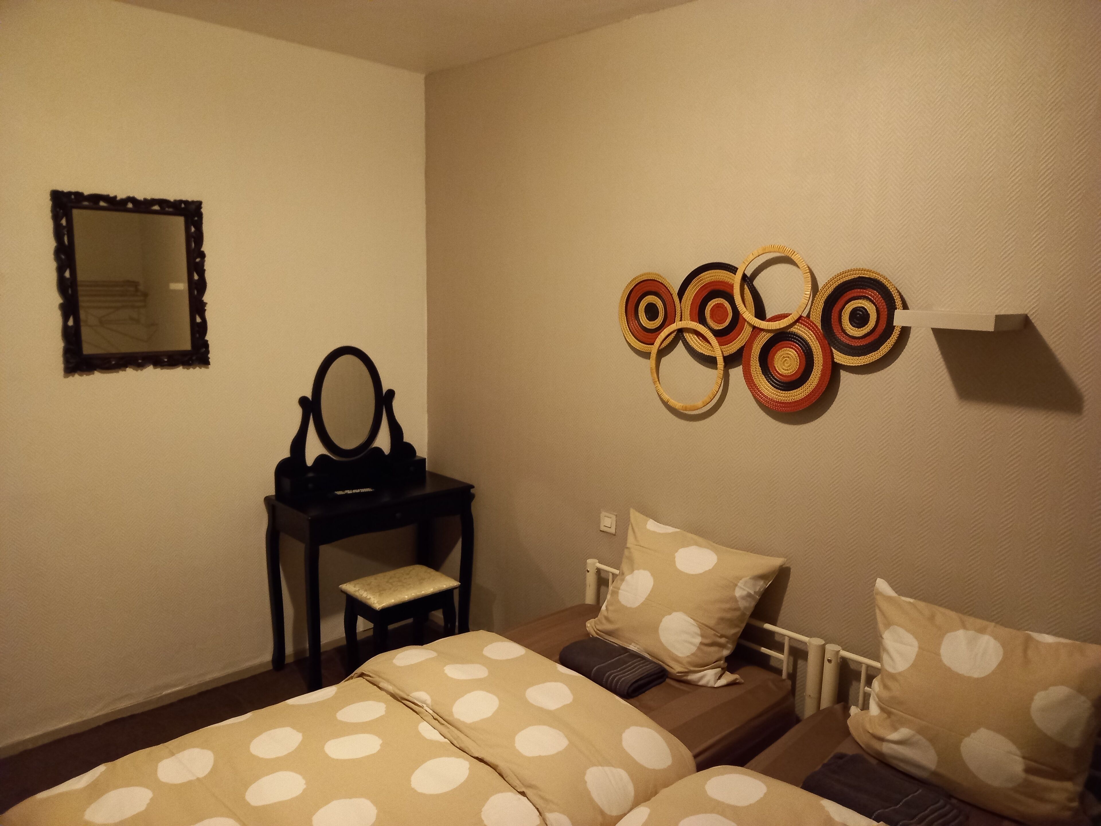 Une chambre avec deux lits, une petite table avec un miroir et un élément décoratif mural.