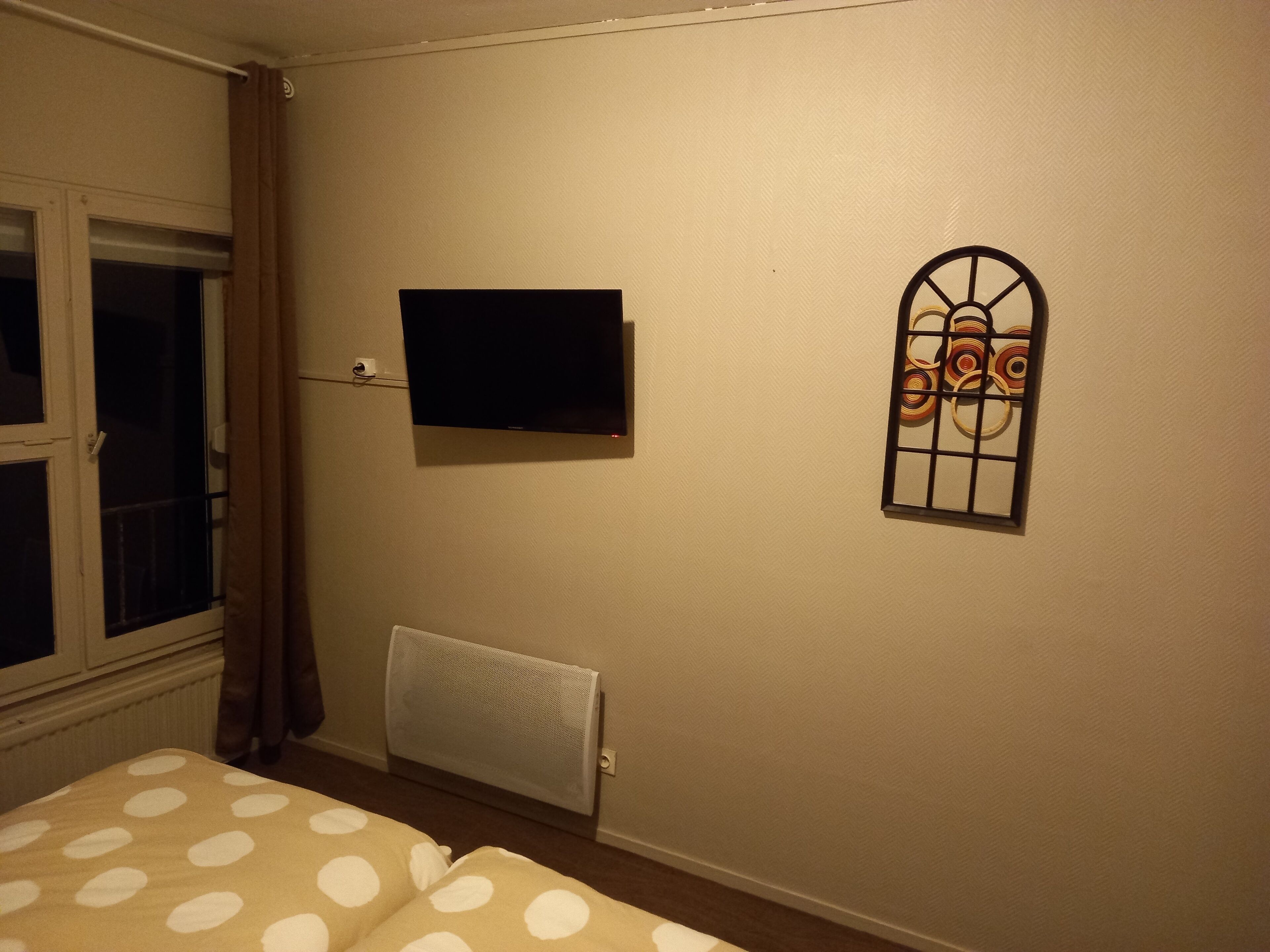 A bedroom with a bed, a window, a wall-mounted TV, and a radiator.