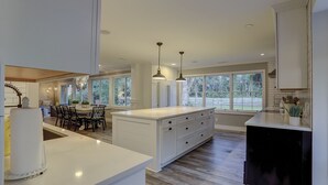 Een ruime keuken met een groot eiland, veel natuurlijk licht door ramen en moderne hanglampen.