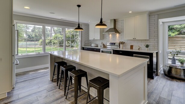 Een moderne keuken met een groot eiland, barkrukken en hanglampen.