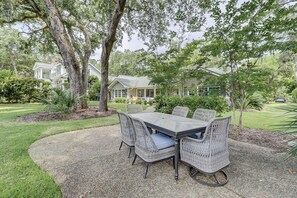 Een terras met een tafel en stoelen, omringd door bomen en een verzorgd gazon.