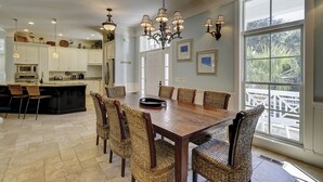 A spacious kitchen with white cabinets, a large island, and a dining area with wicker chairs and a wooden table. - 1 Roadrunner (Hilton Head Island)
