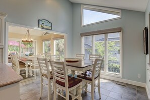 A dining area with a table and chairs, a chandelier, and large windows with a view of greenery. - 6 Dinghy (Hilton Head Island)