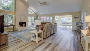 A spacious living room with a fireplace, a ceiling fan, and a dining area with a chandelier. - 6 Dinghy (Hilton Head Island)