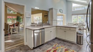 A modern kitchen with white cabinetry, a stainless steel dishwasher, and a large island. There is a dining area with a table and chairs visible through an open doorway. - 6 Dinghy (Hilton Head Island)