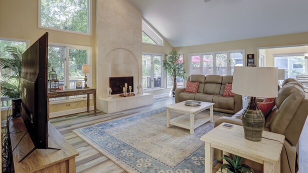 A spacious living room with a fireplace, large windows, a ceiling fan, and a television. - 6 Dinghy (Hilton Head Island)