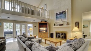 A spacious living room with a grey sofa set, a wooden coffee table, and a fireplace. There is a balcony with a railing and a view of palm trees. - 30 Pelican (Hilton Head Island)