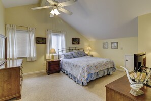 A bedroom with a bed, a nightstand, a dresser, a ceiling fan, and a window with curtains.