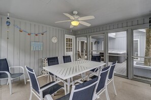 A covered patio with a white table and chairs, a ceiling fan, and a view of a hot tub through a glass door.