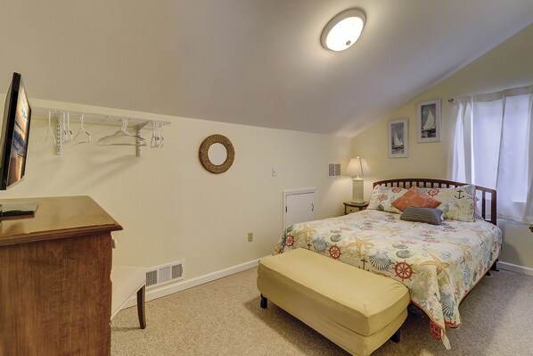 A bedroom with a bed, a desk, a chair, a hanging light fixture, a radiator, and a window with curtains.