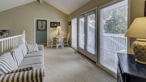 A cozy room with a striped sofa, a dining table with chairs, and large windows with blinds. - 30 Pelican (Hilton Head Island)