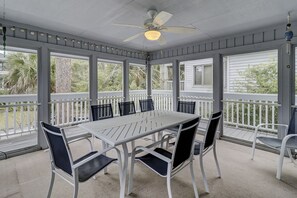 A covered patio with a table and chairs, large windows, and a ceiling fan.
