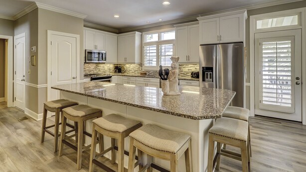 A spacious kitchen with white cabinets, a granite island with bar stools, stainless steel appliances, and a window with blinds. - 1 Sea Oak (Hilton Head Island)