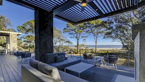Ett takförsett utomhusområde med sittplatser, bestående av en soffa och stolar, med utsikt över en strand.