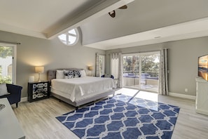 Un dormitorio con cama, mesita de noche, lámpara, ventana grande y vistas al exterior.