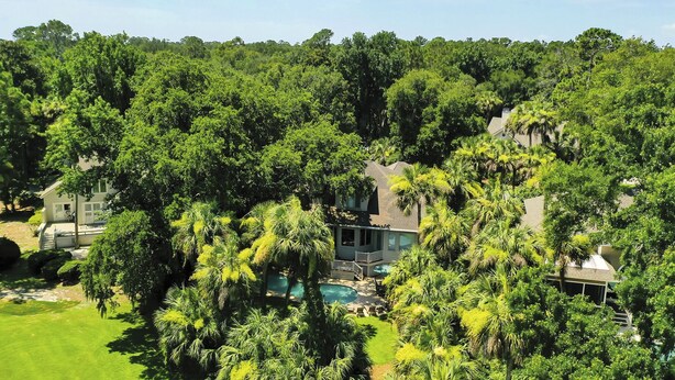 Una casa grande rodeada de abundante vegetación y una piscina.