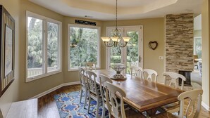 Comedor con una gran mesa de madera, sillas blancas, una araña y una pared decorativa de piedra.