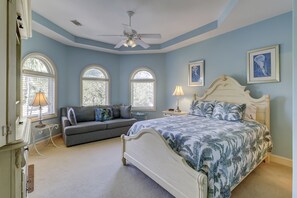 A bedroom with a bed, a sofa, and two windows with arched tops. - 19 Pelican (Hilton Head Island)