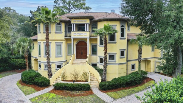 A yellow building with a central entrance, surrounded by palm trees and well-maintained gardens. - 19 Pelican (Hilton Head Island)