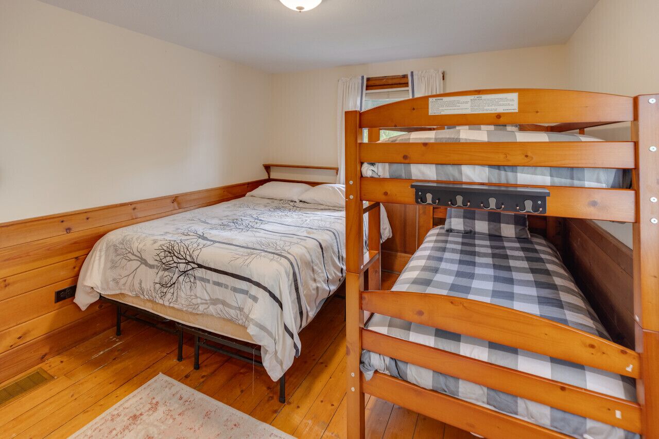 Une chambre avec deux lits superposés en bois, l’un recouvert d’une couverture à carreaux et l’autre d’une couverture à motifs d’arbres.
