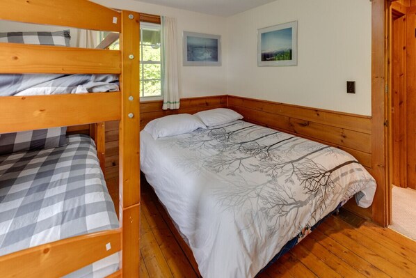 A bunk bed room with a checkered bedspread, a white bedspread with tree branches, and two framed pictures on the wall. - Franconia Notch Retreat- EV Charger (Franconia)