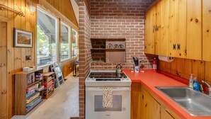 A compact kitchen with a brick wall, wooden cabinets, a white stove, and a red countertop. - Franconia Notch Retreat- EV Charger (Franconia)
