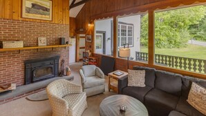 A cozy living room with a fireplace, wicker furniture, and a view of the outdoors. - Franconia Notch Retreat- EV Charger (Franconia)