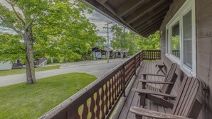 A wooden porch with benches, overlooking a street with houses and a tree. - Franconia Notch Retreat- EV Charger (Franconia)