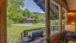 A wooden cabin with a large window overlooking a grassy yard and a house. - Franconia Notch Retreat- EV Charger (Franconia)