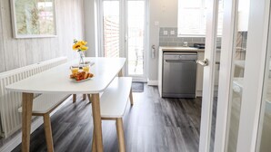 A modern kitchen with a dishwasher, a dining table with chairs, and a view of the outside. - 4 Plas Newydd (Llandudno)