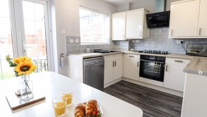 A modern kitchen with white cabinets, a dishwasher, an oven, and a microwave. There is a breakfast setup with croissants and juice on the counter. - 4 Plas Newydd (Llandudno)