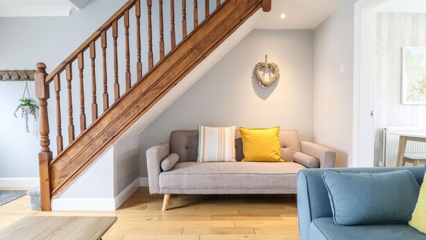 A living room with a wooden staircase, a grey sofa with yellow cushions, a blue sofa, and a wooden coffee table. - 4 Plas Newydd (Llandudno)