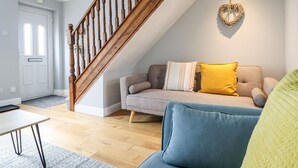 A modern living room with a wooden staircase, a grey sofa with yellow cushions, and a blue armchair. - 4 Plas Newydd (Llandudno)